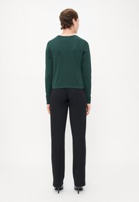 Haut vert à manches longues avec un décolleté rond, design court et texture lisse. Associé à un pantalon noir ajusté et des chaussures à talons.