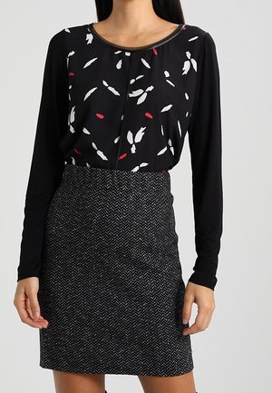 Top negro de manga larga con patrones de hojas rojas y blancas, combinado con una falda lápiz negra texturizada que presenta un patrón de espiga.
