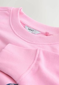 Roze sweatshirt met geribbelde manchetten en halslijn, met een klein merkje met het label "NEXT" aan de achterkant. Zachte katoenen textuur.