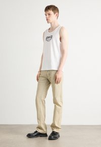 Witte mouwloze tanktop met zwart grafisch patroon, gecombineerd met lichtbeige broek en zwarte schoenen. Eenvoudig, casual ontwerp met een ontspannen pasvorm.