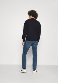 Navy crew-neck sweatshirt with ribbed cuffs, paired with blue straight-leg jeans and white sneakers featuring black accents.