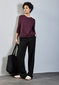 Sudadera granate con texto en relieve "Subtle", combinada con pantalones de pierna ancha negros y zapatillas blancas. Incluye un bolso tote acolchado negro.