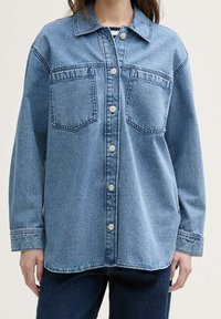 Denimskjorte i lyseblå, med knaplukning foran, to brystlommer og en afslappet pasform med en rund kant og lange ærmer.