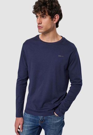 T-shirt a maniche lunghe blu navy in morbido tessuto con scollatura rotonda e dettaglio del logo. Abbinato a jeans in denim azzurro.