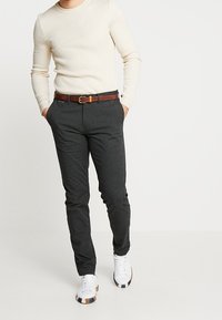 Ribbad krämvit tröja, mörkgrå skräddarsydda byxor, brunt läderbälte och vita sneakers med bruna detaljer. Avslappnad outfit som visar passform och textur.