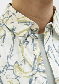 Blomsterbutton-up skjorte med en hvid bund og blå og grønne abstrakte mønstre, glat tekstur og hvide knapper på kraven.