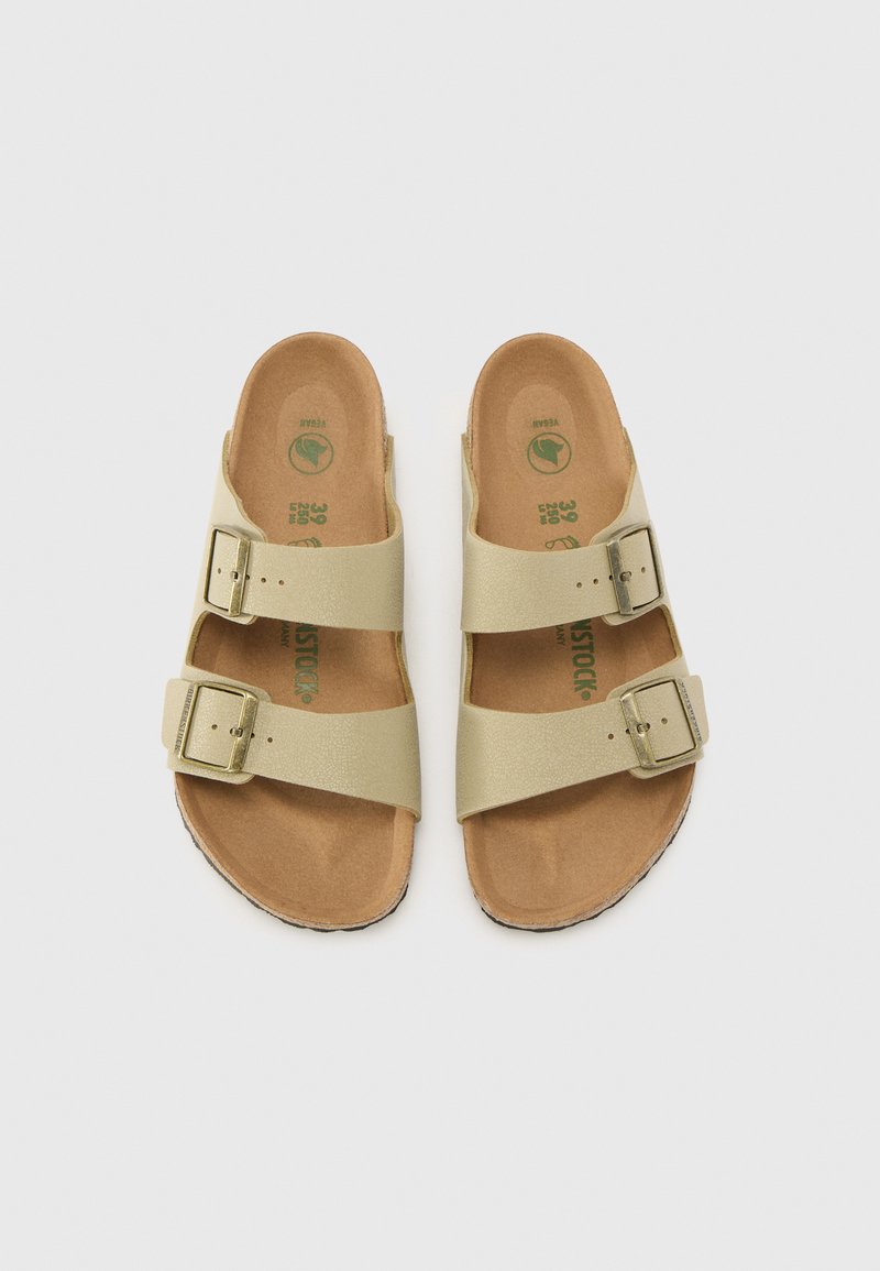 Infradito tan con due fibbie dorate regolabili. Materiale superiore beige testurizzato, soletta morbida e suola in sughero leggermente sagomata.