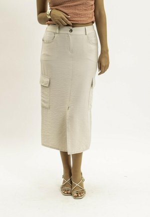 Femme portant une jupe cargo beige mi-longue avec une fente à l'avant, assortie à des sandales à lanières et un haut sans manches texturé.