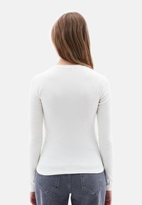 Witte ribbelige top met lange mouwen en een ronde halslijn, gladde textuur en aansluitend ontwerp, gecombineerd met donkergrijze denim jeans.