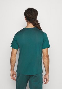 Short-sleeved teal athletic shirt made from breathable material, featuring a round neck, subtle texture, and a contrasting white accent on the sleeve.