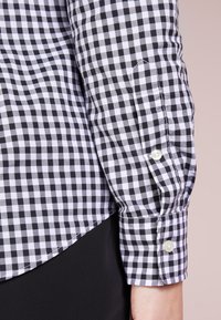 Tessuto della camicia a scacchi in bianco e nero con una vestibilità slim. Polsino abbottonato e dettaglio dell'orlo curvo. Texture in cotone liscia.