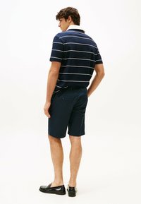 Polo a righe blu con linee bianche, maniche corte e colletto bianco a contrasto, abbinato a pantaloni corti blu e mocassini neri.