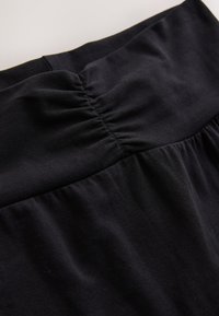 Gros plan d’un tissu noir avec un détail de couture froncée, montrant la texture et les plis d’un matériau doux et extensible.