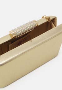 Gold clutch purse featuring a textured metallic finish, adorned with a jeweled clasp. The interior is lined with fabric and includes compartments.
