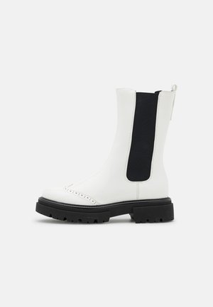 Białe skórzane botki za kostkę z czarnymi elastycznymi panelami bocznymi, czarną gumową podeszwą, zaokrąglonym noskiem i dekoracyjnymi perforacjami wzdłuż czubka.