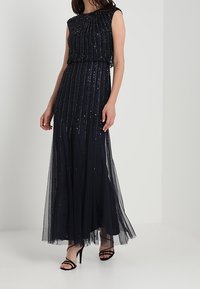 Vestido largo azul marino con intrincados detalles de cuentas, corsé ajustado y falda de tul fluida. Presenta un diseño sin mangas y una textura en capas.