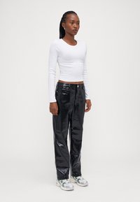 Black faux leather pants with a crocodile texture and relaxed fit, paired with a white long-sleeve fitted top and white sneakers.