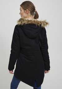 Black parka with a faux fur-lined hood, waist tie, and a slightly longer back. Features a smooth texture and a relaxed fit.