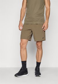 Ελαιόχρωμα σορτς με χαλαρή εφαρμογή, ελαφρύ ύφασμα και κεντητό λογότυπο. Συνδυασμένα με ένα αντίστοιχο αμάνικο τοπάκι και μαύρα αθλητικά παπούτσι�α.