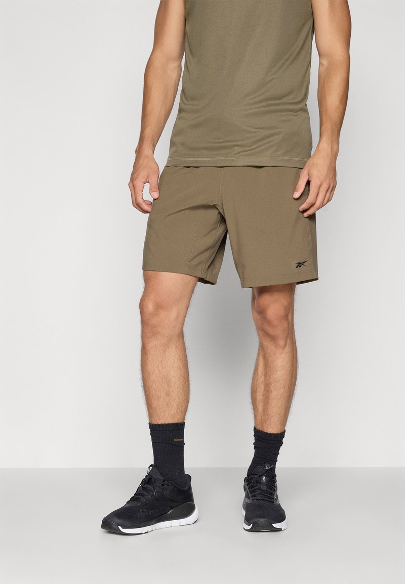 Ελαιόχρωμα σορτς με χαλαρή εφαρμογή, ελαφρύ ύφασμα και κεντητό λογότυπο. Συνδυασμένα με ένα αντίστοιχο αμάνικο τοπάκι και μαύρα αθλητικά παπούτσια.