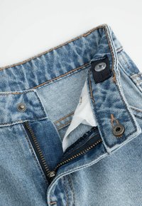 Jasnoniebieskie dżinsy z zamkiem błyskawicznym, metalowym zapięciem na guzik oraz kontrastowym szwem. Wewnętrzny materiał widoczny w talii.