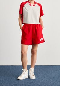 Červené sportovní kraťasy s elastickým pasem a bílým logem Nike; kombinované se šedým a červeným krátkým rukávem. Bílé vysoké tenisky.