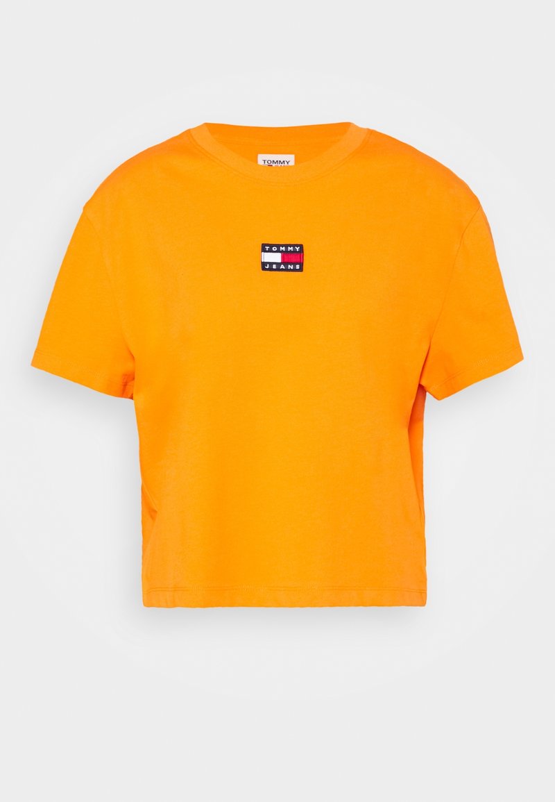 Oranssi lyhythihainen t-paita, joka on valmistettu puuvillasta ja jossa on pyöreä kaula-aukko. Edessä on pieni Tommy Jeans -logopatchi mustassa, punaisessa ja valkoisessa.
