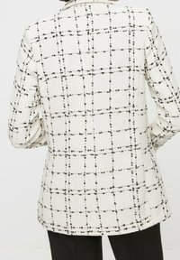Blazer bianco a quadri con tessuto testurizzato, caratterizzato da un motivo a griglia nera, maniche lunghe e un taglio leggermente allungato.