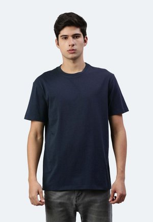 Maglietta di cotone blu navy con colletto a girocollo, maniche corte, orlo dritto e texture uniforme. Indossata con jeans grigi.