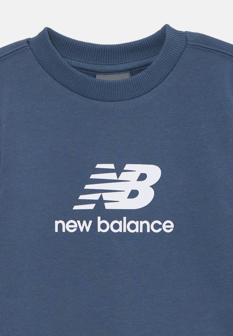 Sudadera azul con cuello redondo acanalado, hecha de un tejido suave, con un logotipo y texto de New Balance en blanco impresos en la parte delantera.