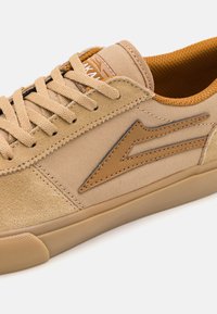 Tan sneakers with a mix of suede and canvas. Features rounded toe, lace-up design, and a contrasting tan logo. Textured rubber sole.