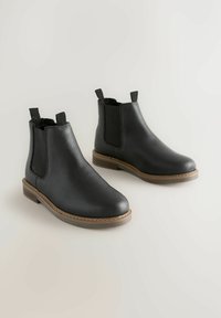 Schwarze Leder-Stiefeletten mit elastischen seitlichen Einsätzen, abgerundeter Zehenpartie, sandfarbener Gummisohle und gesteppten Details entlang der Sohlenkante.