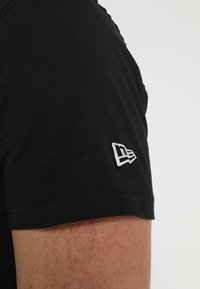 T-shirt in cotone nero con collo rotondo, caratterizzato da un logo ricamato bianco sulla manica sinistra. Tessuto morbido e maniche corte.