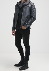 Grijze leren motorjas met geribbelde schouderaccenten, open ritssluiting, gedragen over een zwart shirt, gecombineerd met zwarte slim-fit spijkerbroek en laarzen.