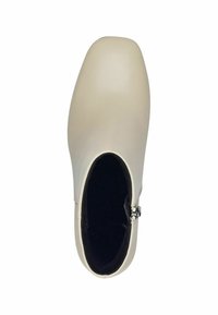 Botín beige hasta el tobillo con un exterior liso, punta redondeada, tacón bajo y detalle de cremallera lateral; forro interior negro y diseño minimalista.