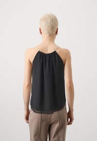 Satin svart topp med tynne perlestrikker, innsamlet halslinje og løs passform, kombinert med beige bukser. Glatt tekstur og lett design.