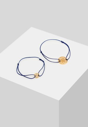 Bracciali in metallo color oro con cordino blu, caratterizzati da design circolari intagliati. Un bracciale è più grande e presenta una perlina decorativa; l'altro è più piccolo.