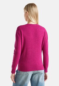 Růžový pletený svetr s kulatým výstřihem, žebrovanými manžetami a lemem. Měkká textura, volný střih a viditelné švy na ramenou.
