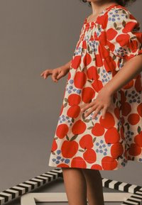 Vestido de algodón con estampado de manzanas rojas y azules, con mangas cortas abullonadas y escote fruncido. El vestido llega a la altura de la rodilla.