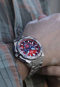 Orologio in acciaio inossidabile argento con quadrante rosso e nero, dotato di tre sottoquadranti, grandi indicatori delle ore e bracciale in metallo.