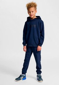 Marineblauwe hoodie met gedrukt logo, gecombineerd met bijpassende joggers. De capuchon is gevoerd en de mouwen hebben elastische boorden. Het schoeisel heeft een contrasterende zool.