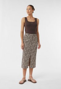 Brązowy top na ramiączkach w zestawieniu ze spódnicą w panterkę o średniej długości, z dekoltem z przodu, noszoną z złotymi sandałami na paski na jednolitym tle.