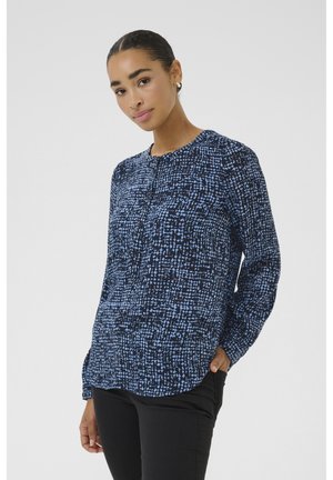 Chemise à manches longues bleu marine avec un motif abstrait texturé en bleu, encolure arrondie et détails de boutons, associée à un pantalon noir ajusté.