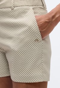 Μπέζ σορτς με γεωμετρικό μοτίβο, πλαϊνές τσέπες και διακριτική λεπτομέρεια λογότυπου κοντά στη μέση. Ομαλή υφή υφάσματος.