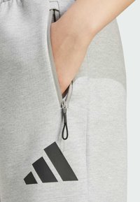 Jogging grigi con tasca con zip, con logo Adidas nero. Tessuto morbido con una trama liscia e design leggero.