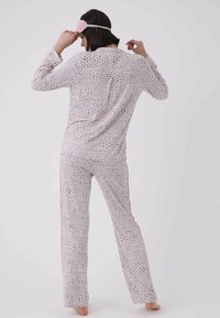 Långärmad, prickig pyjamasuppsättning i ljusrosa och svart. Mjukt tyg med lös passform, röda sidostreck och en matchande sovmask.