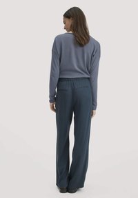 Blauwe langslieving top, gecombineerd met marineblauwe wijde broek. Soepele stof, relaxte pasvorm, elastische tailleband en achterzakken op de broek.