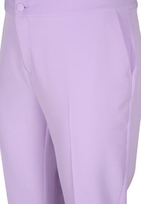 Närbild av ljuslila skräddarsydda byxor med knappmidja och sidofickor, som visar den släta tygtexturen och sömnadsdetaljer.