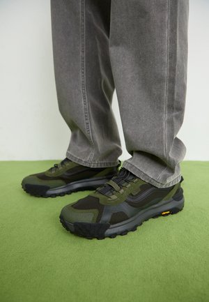 Tenis pretos e verdes com uma superfície texturizada, uma combinação de malha e materiais em borracha, e uma sola robusta, concebidos para durabilidade.