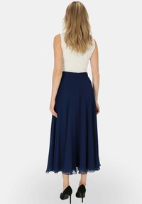 Granatowa spódnica midi w plisy z dopasowaną talią, zwiewnym materiałem i przezroczystym detalem na hemie, w połączeniu z białym topem bez rękawów i czarnymi szpilkami.